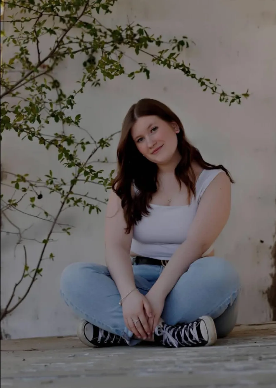 Makayla Barnett smiling, sitting cross-legged in front of a white wall